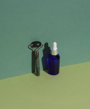 Yeşil zemin üzerinde yüz serumu şişesi ile Jade masaj silindiri