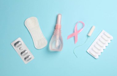 Women's health concept. Vaginal enemas, pad, tampon and pink awareness ribbon on blue background. Flat lay clipart