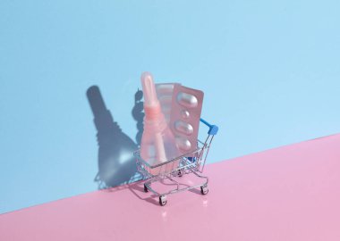 Mini supermarket trolley with vaginal enema, pills on blue pink background. Women Health clipart