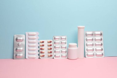 Çeşitli ilaçlar, mavi-pembe arka planda su toplayan haplar. Yaratıcı düzen, minimalizm tıp konsepti