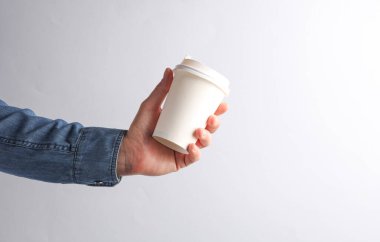 Kot gömlekli bir adam gri arka planda beyaz, boş bir kahve fincanı tutuyor.