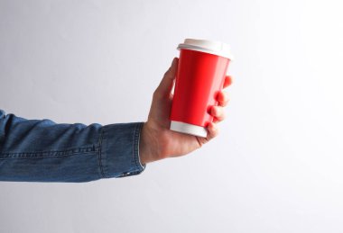 Kot gömlekli bir adam gri arka planda kırmızı, boş bir kahve fincanı tutuyor.
