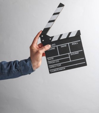 Adamın eli kot gömlekli, elinde gri arka planda film klaketi var.