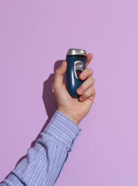 Mor renkli arka planda gölgeli elektrikli tıraş makinesi tutan bir adam.