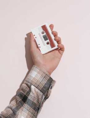 Adamın eli gömlekte, elinde bej arka planda ses kaseti var, gölgesi de var.