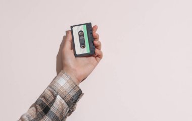 Adamın eli gömlekte, elinde bej arka planda ses kaseti var, gölgesi de var.