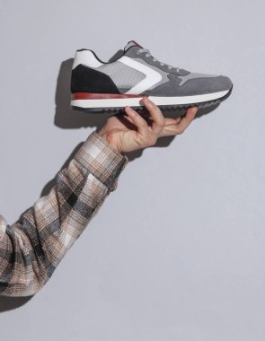 Gri arka planda spor ayakkabısı tutan adamın eli tişörtlü gölgesi