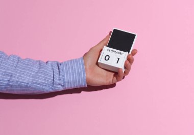 Adamın eli gömlekli, tahta bloklu takvim düzenleyicisi ile 1 Şubat 'ta pembe arka planda, gölgeli.