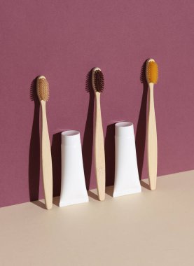 Eko ahşap diş fırçaları ve bordo bej arka planda gölgeli diş macunu tüpleri. Güzellik konsepti