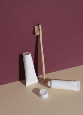 Eko ahşap diş fırçası ve bordo bej arka planda gölgeli diş macunu tüpleri. Güzellik konsepti