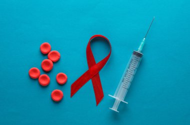 Şırınga ve kırmızı HIV, AIDS farkındalık kurdelesi, mavi zemin üzerinde kırmızı kan hücreleri.