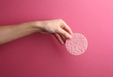 Makyaj çıkarıcı sünger pembe arka planda kadın elinde.