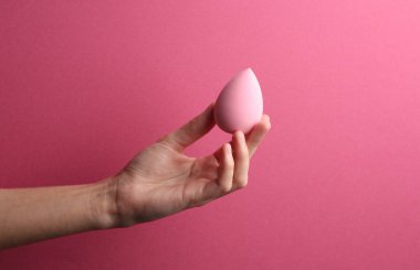 Pembe arka planda kadın elinde makyaj süngeri blenderi