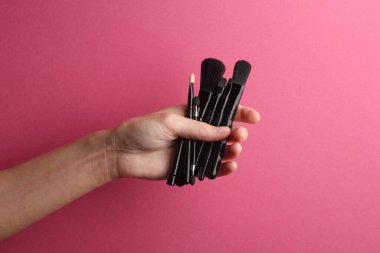 Siyah makyaj fırçaları pembe arka planda kadın eline yerleştirilmiş.