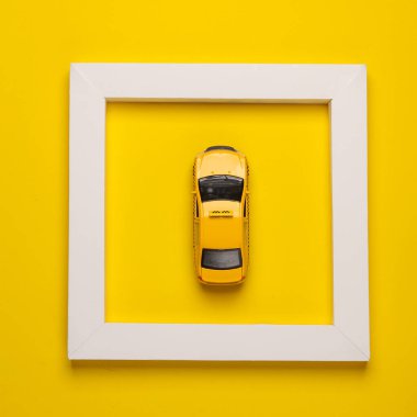 Sarı arka planda beyaz çerçeveli oyuncak taksi. Yaratıcı düzen. Minimalizm