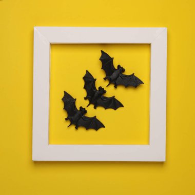 Sarı arka planda beyaz çerçeveli plastik yarasalar. Yaratıcı düzen. Cadılar Bayramı. Minimalizm