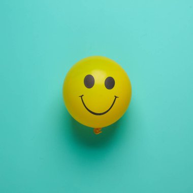 Mavi arka planda gülen yüzlü sarı balon. Yaratıcı düzen. Minimalizm