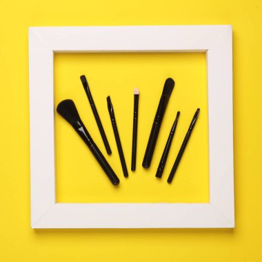 Sarı arka planda çerçeveli makyaj fırçaları. Güzellik konsepti