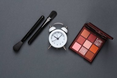 Güzellik malzemeleri, makyaj malzemeleri ve koyu bir arka planda çalar saat. Düz yatıyordu