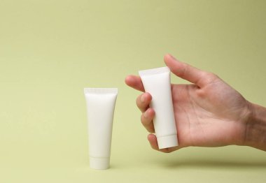 Yeşil arka planda beyaz krema tüpünü tutan el. Tasarım şablonu, model. Güzellik konsepti