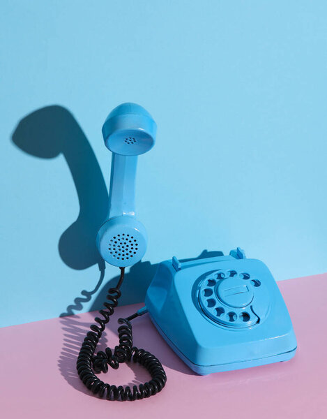 Синий вращающийся ретро телефон с плавающим трубкой на розовом голубом фоне с тенью. Креативная планировка