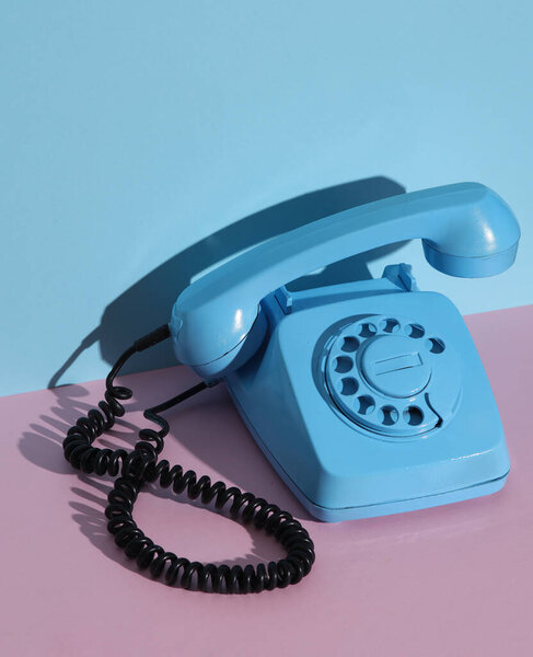 Blue Rotary retro rotary telephone with floating handset on pink blue background with shadow. Creative layout
