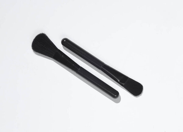 Two black make-up brushes on white background with shadow