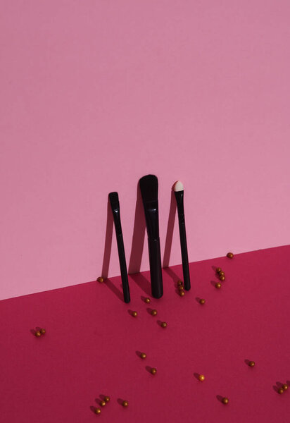 Black make-up brushes with powder balls on pink background. Beauty concept