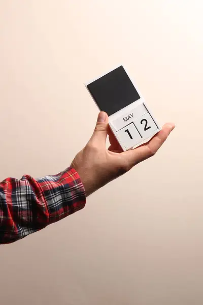 Stock image Date May 12, block calendar in male hand on beige background