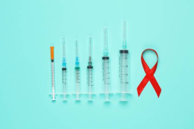Kırmızı AIDS farkındalık kurdelesi ve mavi arka planda şırıngalar. Tıp konsepti
