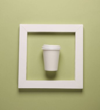 Beyaz kare çerçeveli, yeşil arka planlı kahve fincanını çıkar. Estetik asgari natürmort. Kavramsal fotoğraf. Üst görünüm