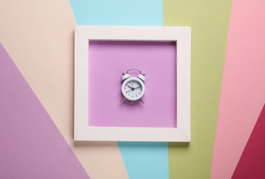 Renkli arkaplanda beyaz kare çerçeveli çalar saat. Estetik asgari natürmort. Kavramsal fotoğraf. Modern sanat. Üst görünüm