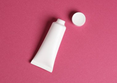 Pembe arka planda beyaz krema tüpü açılmış. Üst görünüm