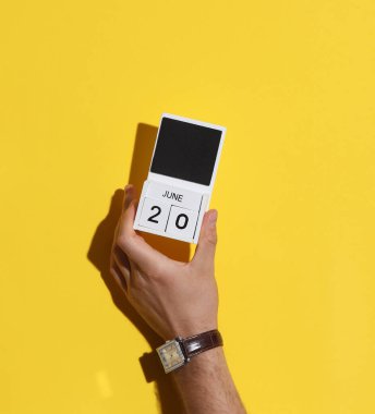 20 Haziran tarihli ahşap blok takvimi sarı arka planda tutan adamın eli