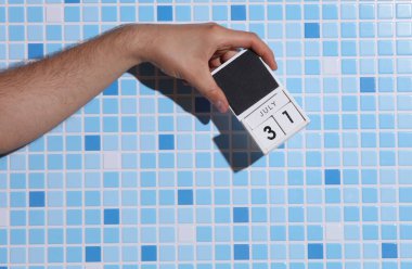 31 Temmuz tarihli ahşap blok takvimi tutan adamın eli fayans zemininde