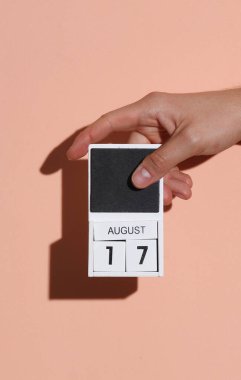 17 Ağustos tarihli ahşap bloklama takvimi pembe parlak arkaplanlı bir adamın elinde.