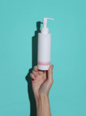 Bir kadının elinde mavi arka planda bir gölgesi olan krema şişesi var.