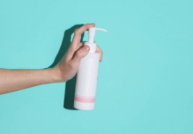 Bir kadının elinde mavi arka planda bir gölgesi olan krema şişesi var.