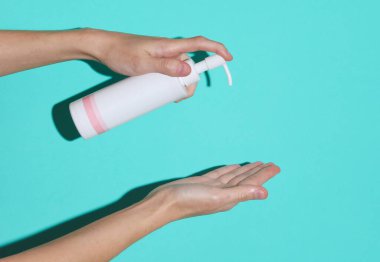 Bir kadının elinde mavi arka planda bir gölgesi olan krema şişesi var.