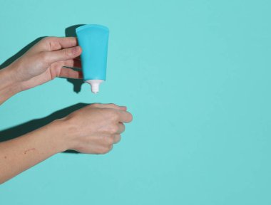 Kadınların elleri mavi arka planda şişeden krem sürerler.