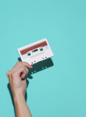 80 'lerin retro ses kasedini elinde tutan bir kadın. Mavi arka planda, gölgeli.