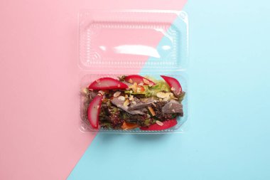 Pembe arka planda plastik bir kutuda salatalar. Tekaway yemeği. Üst görünüm