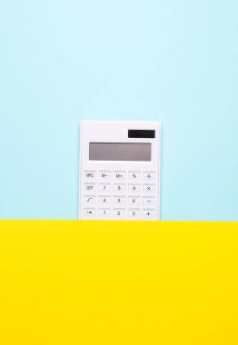 Beyaz hesap makinesi mavi sarı kağıttan dışarı bakıyor. Yeni fikir, iş kavramı