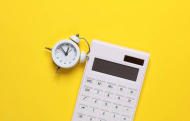 Sarı arka planda çalar saati olan bir hesap makinesi. Vakit nakittir. İş konsepti. Üst görünüm