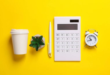 Hesap makinesi, çalar saat, kalem, kahve fincanı ve sarı arka planda bitki. İş konsepti. Çalışma alanı. Üst Manzara. Düz yatıyordu
