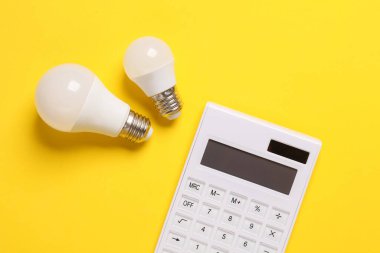 Sarı arka planda kurşun ampulleri olan hesap makinesi. Enerji tasarrufu