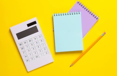 Sarı arkaplanda not defterleri olan hesap makinesi