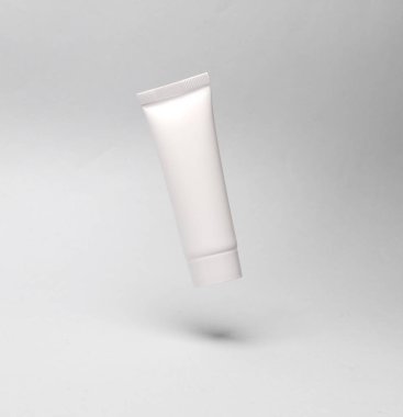 Beyaz krema tüpü gri arka planda havada duruyor. Model, tasarım şablonu