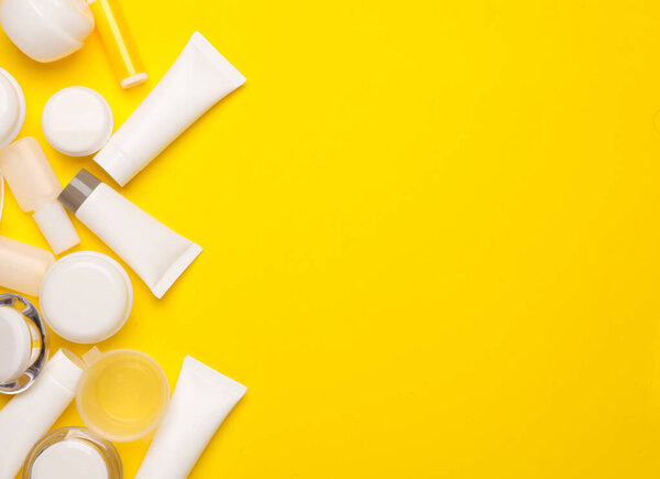 Tubes and jars of cream on a yellow background. Beauty products. Top view. Copy space