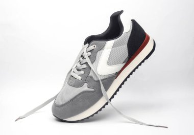 Beyaz arka planda bağcıkları çözülmüş gri bir spor ayakkabı.